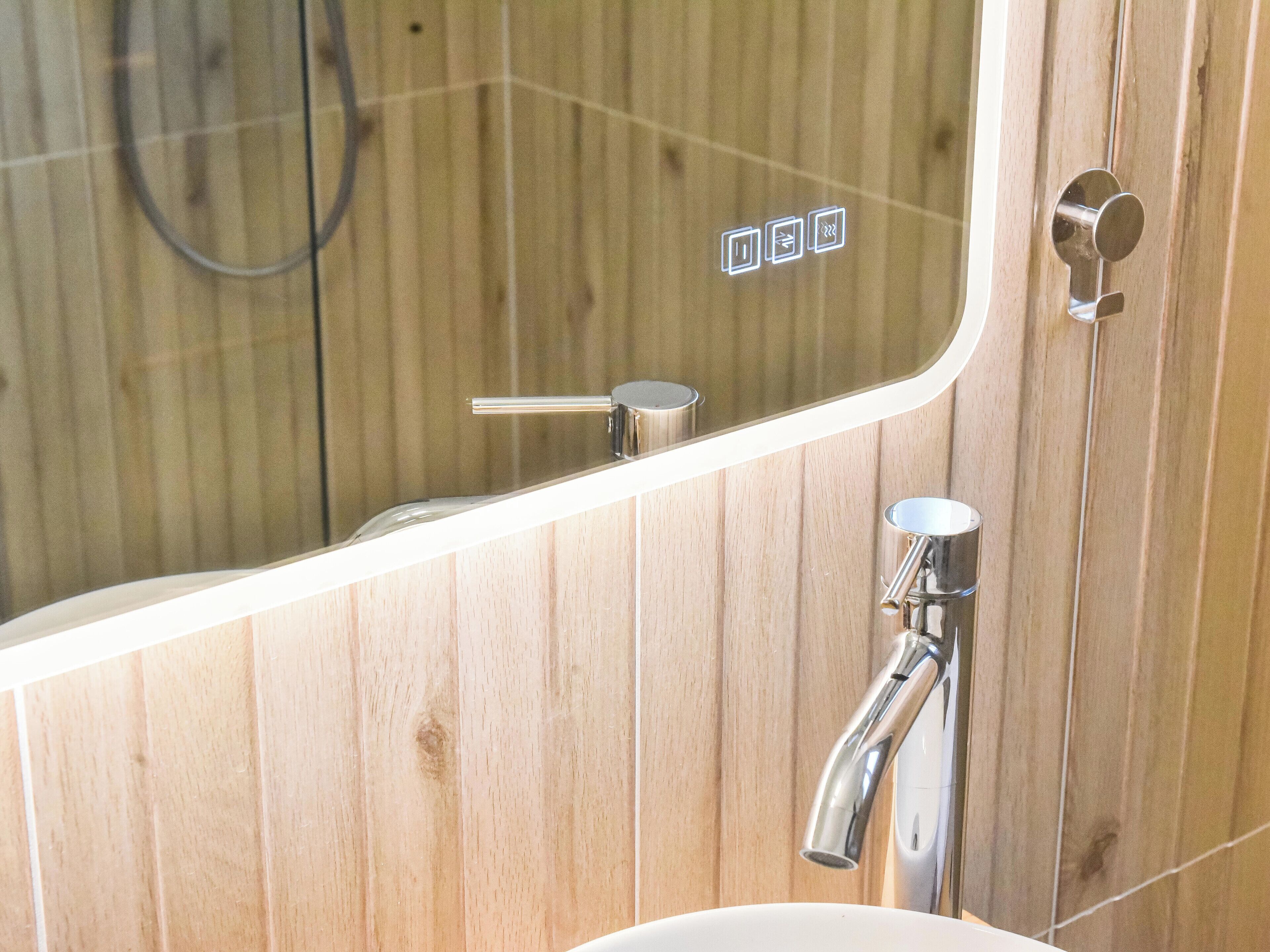 Ein Badezimmer mit Holzwand, einem Spiegel, einem Waschbecken und einer Duschkabine.