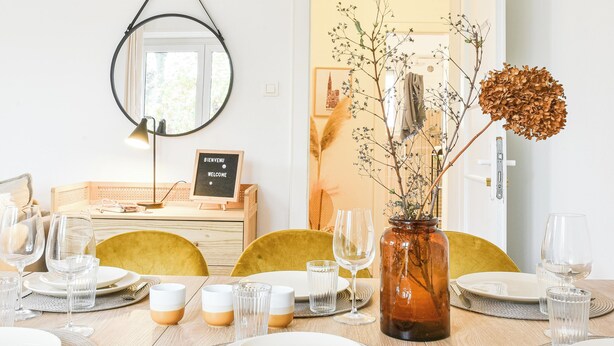 A dining area with a wooden table set for four, a vase with dried flowers, and a welcome sign. - Rock in Share - Bianca – 2-Bedroom Apartment with Parking Included & Tram (Strasbourg)