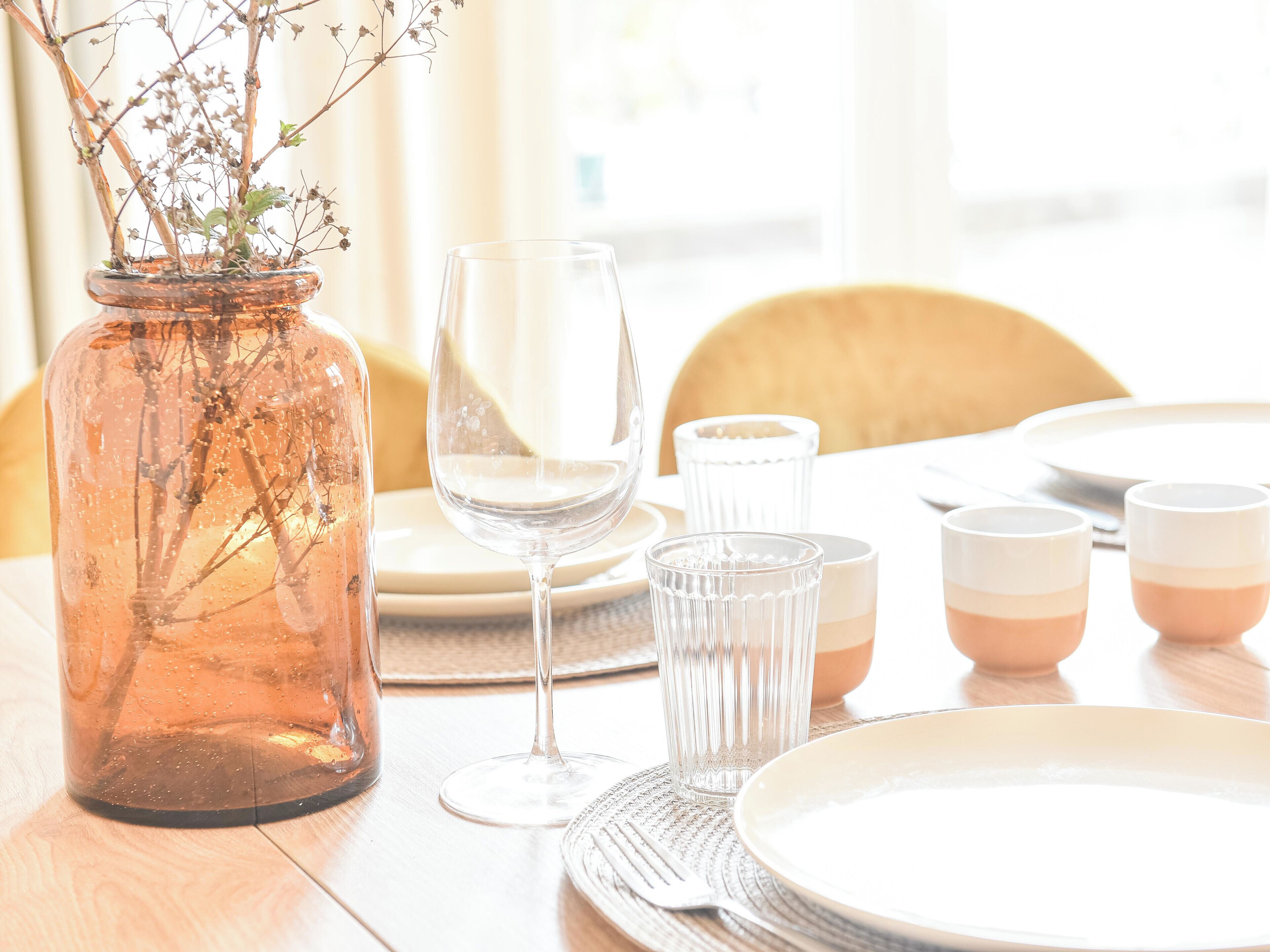 Une table à manger avec un vase, un verre à vin et des assiettes.