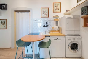A compact kitchen with a sink, a washing machine, and a dining area with two chairs.