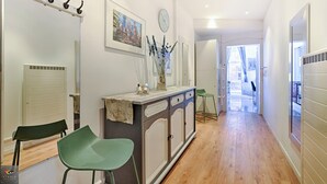 A hallway with a mirror, a clock, a vase with dried flowers, and a green chair. - La Pépite Place Mondon pour voir le PAPE du balcon (Metz)