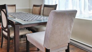 Uma área de refeições com mesa de vidro, quatro cadeiras e uma janela com cortinas leves.
