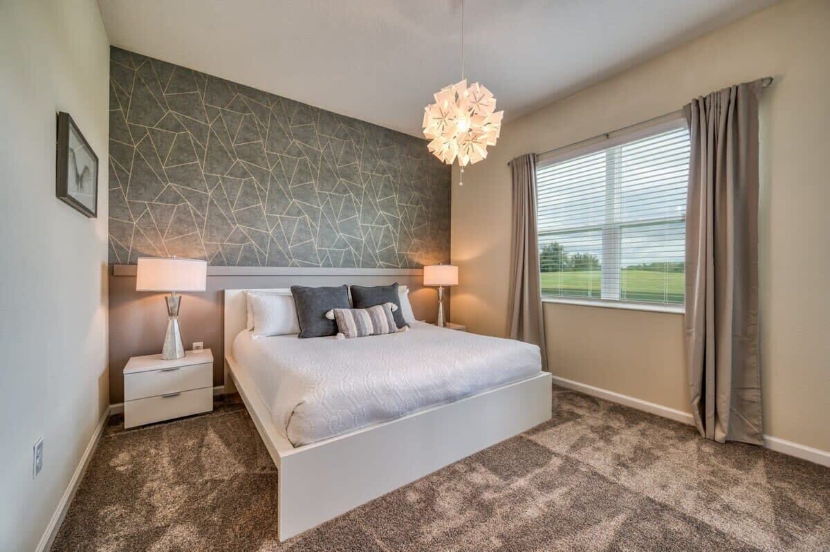 A bedroom with a large bed, two bedside tables with lamps, a geometric wall pattern, and a window with curtains.