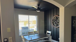 A dining area with a table, chairs, a bench, a ceiling fan, a window with blinds, and a decorative wall piece. - Little Peace and Quiet out on Little Leaf (San Tan Valley)