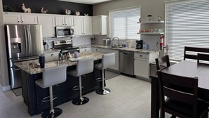 A modern kitchen with white cabinets, stainless steel appliances, a granite countertop, and a bar area with stools. - Little Peace and Quiet out on Little Leaf (San Tan Valley)
