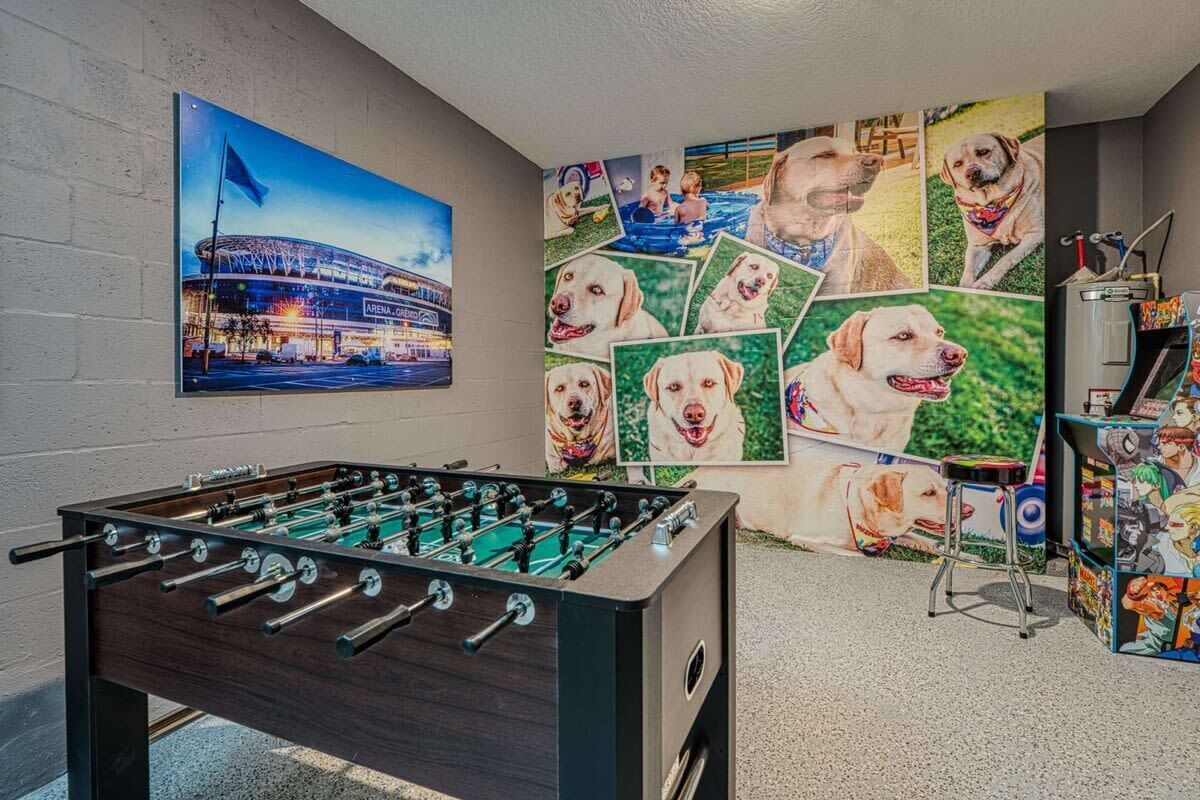 Ein Zimmer mit einem Tischfußballtisch, einer Wand mit einem Stadionfoto und einer Wand mit mehreren Hundebildern.