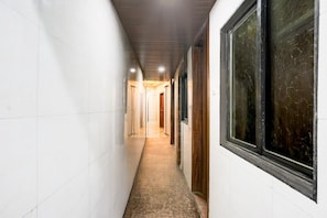 A corridor with white walls, a tiled floor, and large windows with wooden frames.