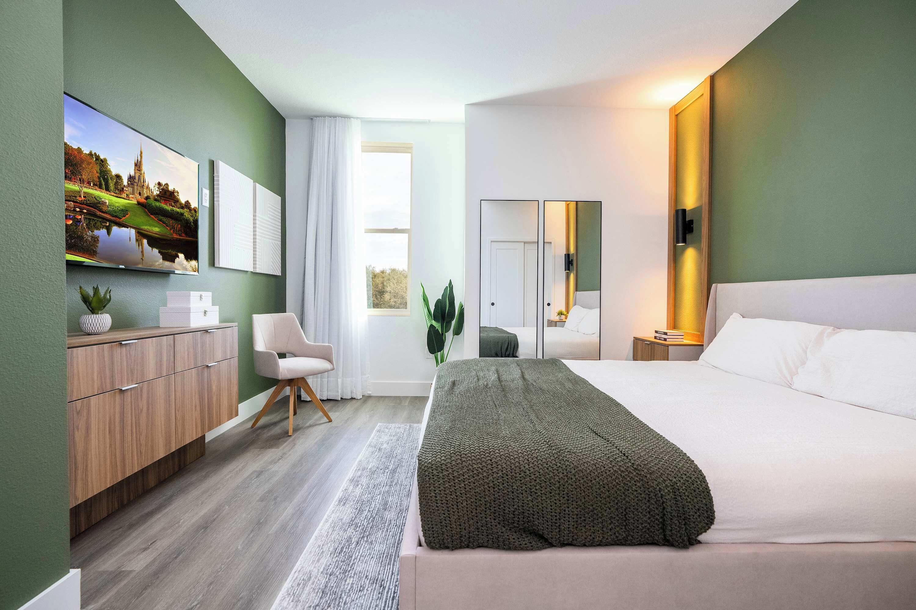 Una habitación de hotel moderna con una cama grande, un aparador de madera, una silla, un ventanal y un cuadro en la pared.
