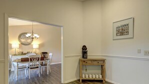 A dining area with a table and chairs, a chandelier, a coffee table with a clock, and a framed picture on the wall.