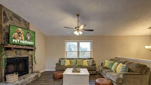 A pet-friendly living room with a fireplace, two couches, a ceiling fan, and a television displaying a dog.