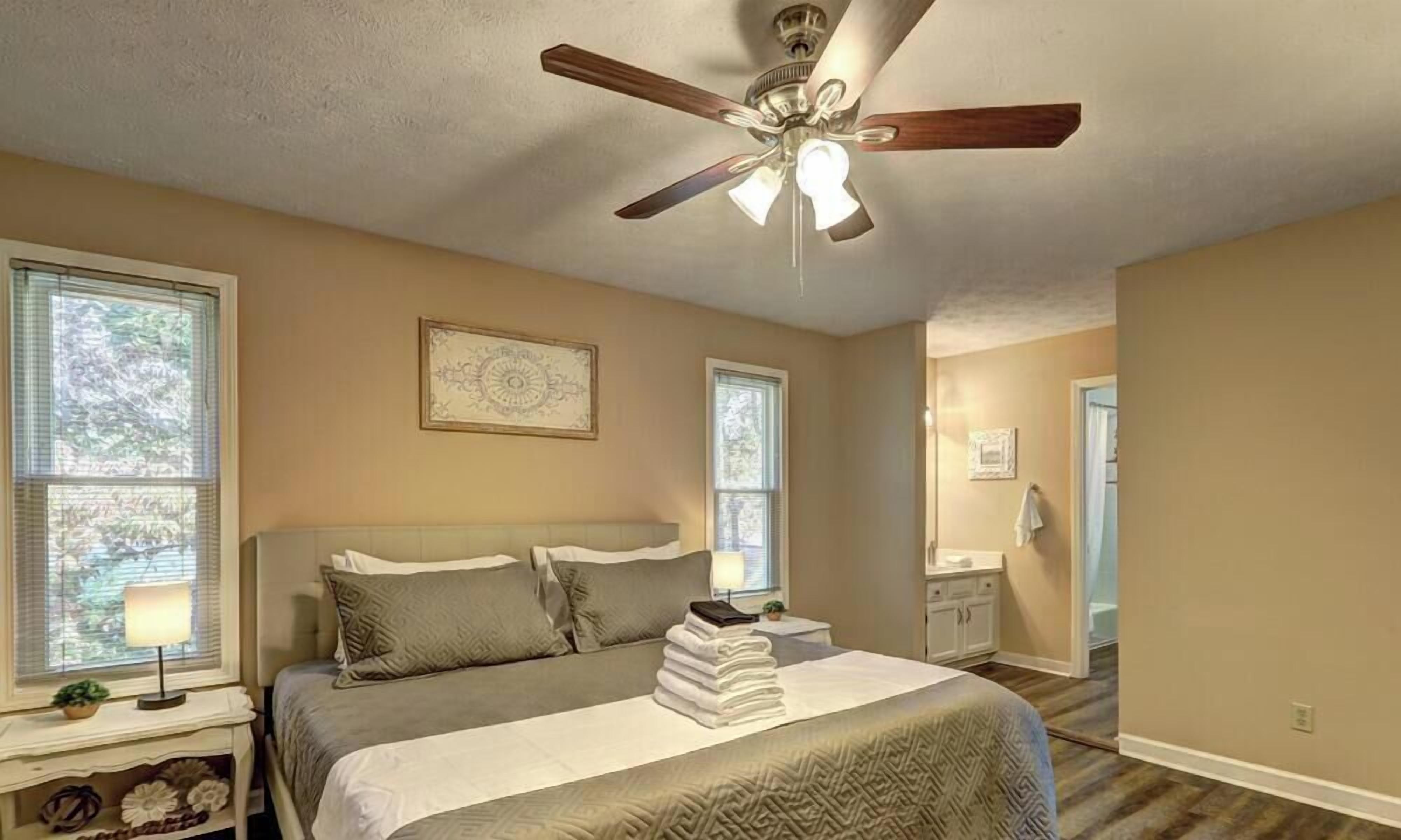 A bedroom with a bed, a ceiling fan, a nightstand, a lamp, and a window.
