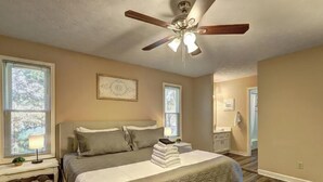 A bedroom with a bed, a ceiling fan, a nightstand, a lamp, and a window.