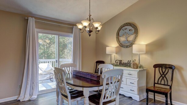 A dining area with a chandelier, a table, chairs, a dresser, and a window with curtains.