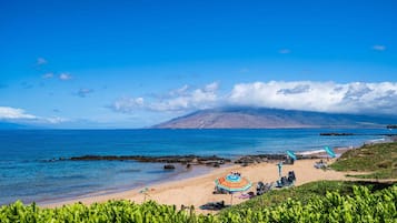A beach with clear skies, a mountain in the background, and a few umbrellas.