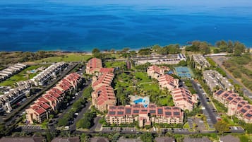 An aerial view of a coastal hotel with multiple buildings, a swimming pool, and a view of the ocean.