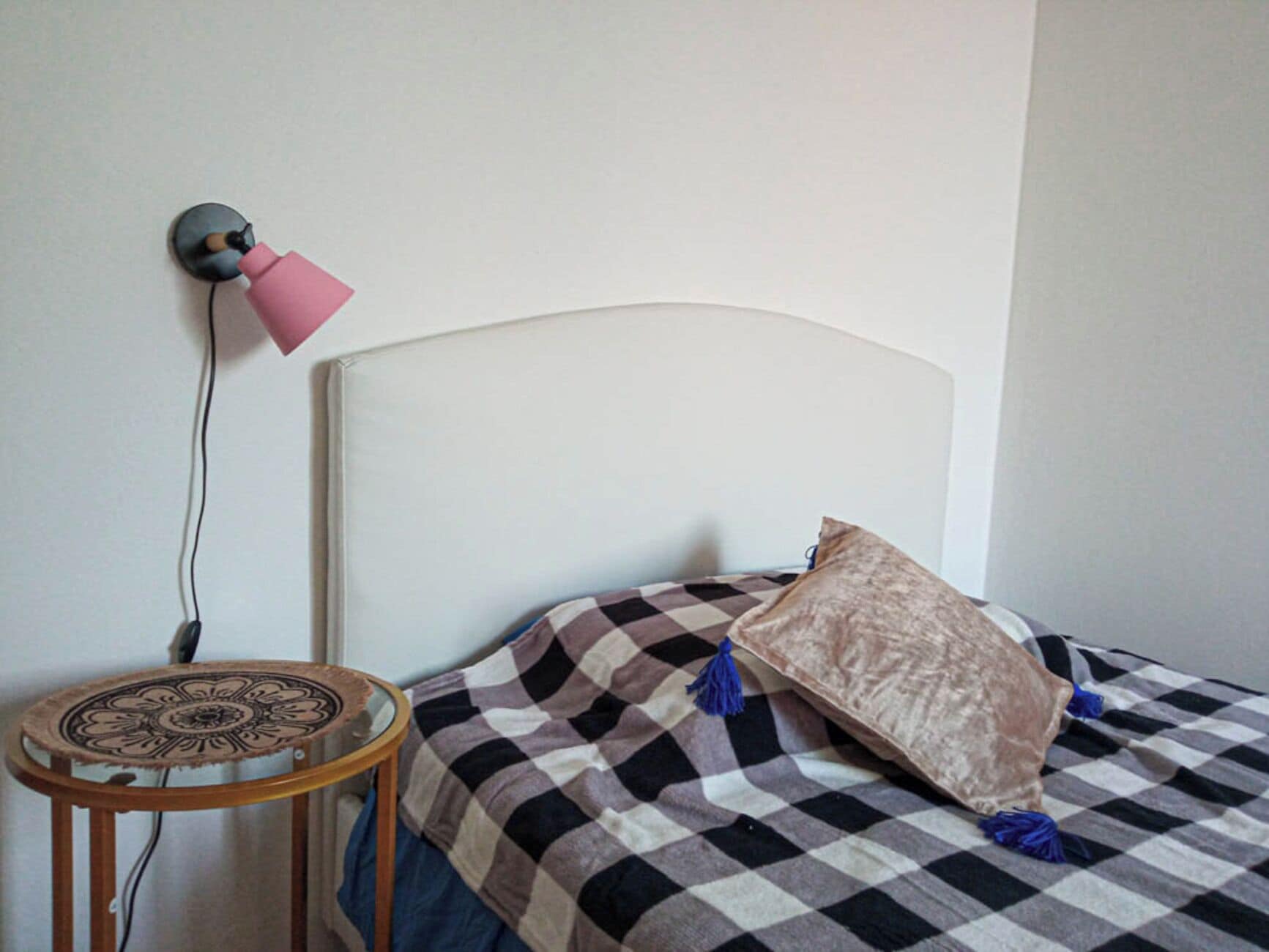 A room with a bed, a round table, and a wall-mounted lamp.