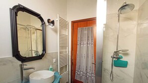 A bathroom with a sink, mirror, towel rack, shower, and a door with a curtain.