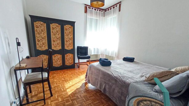 A room with a bed, a desk, a chair, a wardrobe, and a window with curtains.