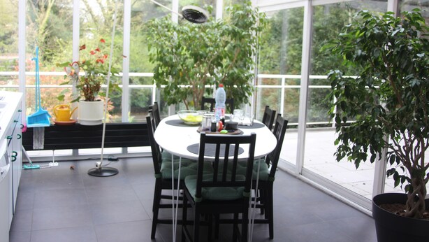 A conservatory with a round table, chairs, and potted plants.