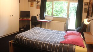 A bedroom with a bed, desk, chair, and a window with curtains.