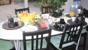 A round dining table with chairs, a bowl of oranges, a bottle of water, a thermos, and various breakfast items.