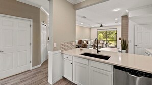 Una cocina moderna con armarios blancos, un lavavajillas de acero inoxidable y un amplio ventanal con vistas al exterior.