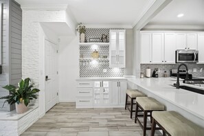 A modern kitchen with white cabinetry, a herringbone tile backsplash, and a central island with stools. - Casa de Maggie - Peaceful, Updated 3 Bedroom townhome in Quiet Neighborhood (Bradenton)