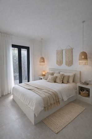 Ein Schlafzimmer mit einem großen Bett, Nachttischlampen, einem gewebten Teppich und Blick durch ein Fenster.