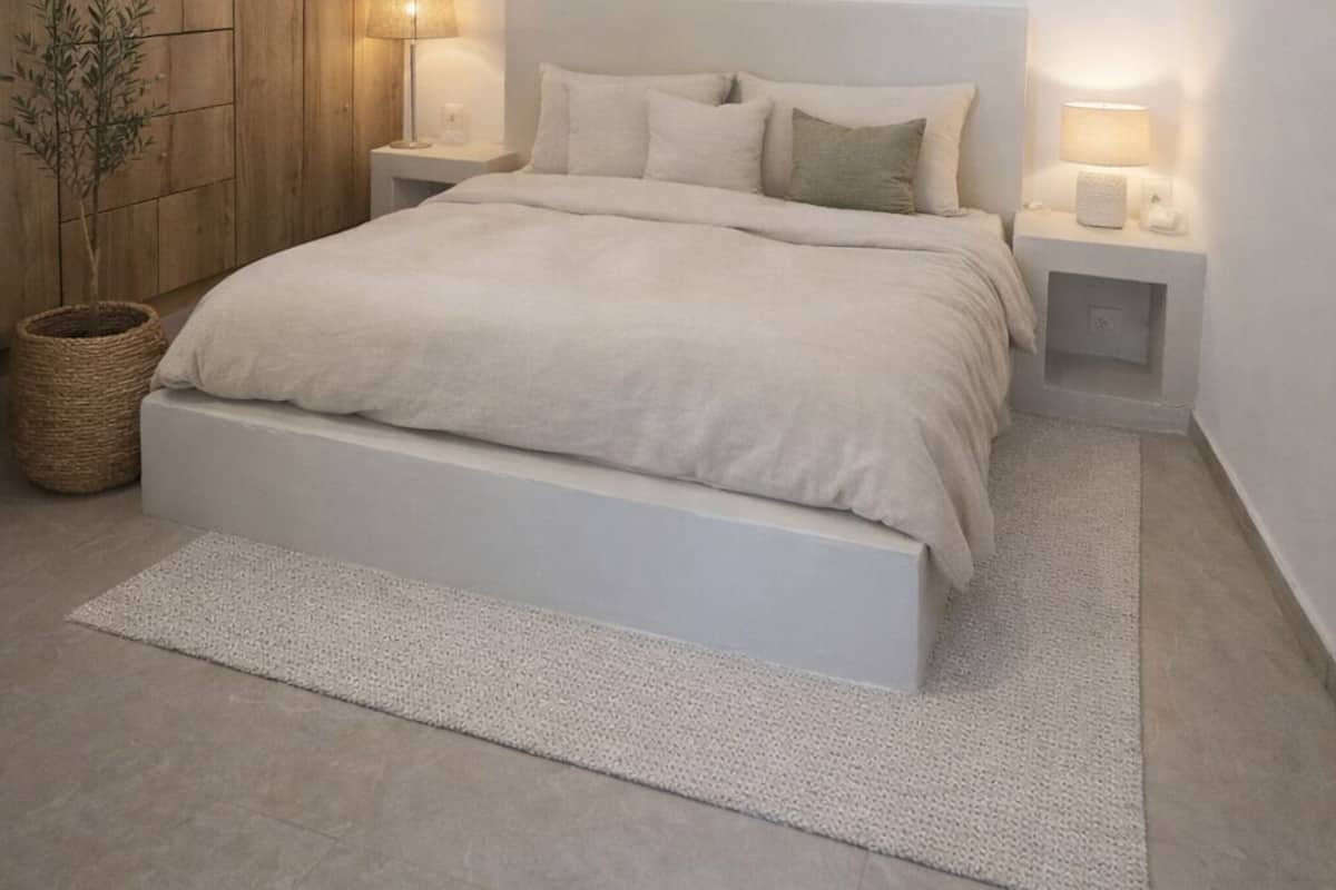 A bedroom with a bed, bedside lamps, a wall-mounted artwork, a wooden panel wall, and a potted plant.