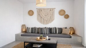 Un salon moderne avec un canapé gris, des coussins à motifs, une décoration murale en macramé tissé et un luminaire suspendu.