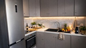 Une cuisine moderne avec des armoires grises, un réfrigérateur en acier inoxydable, un four encastré, un évier avec un robinet et un plan de travail sur lequel se trouvent divers objets.