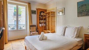 A hotel room with a bed, a wooden bookshelf, a chair, and a window with curtains. - Paris Center St Claude residence (Paris)