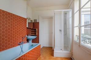 Un baño con pared de patrón hexagonal, un lavamanos azul, una ducha y una ventana con vistas.