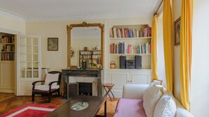 A living room with a fireplace, bookshelves, a sofa, and a dining table. - Paris Center St Claude residence (Paris)