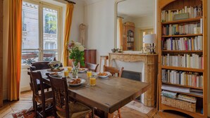 A dining area with a wooden table, chairs, a bookshelf, and a view of the outside. - Paris Center St Claude residence (Paris)