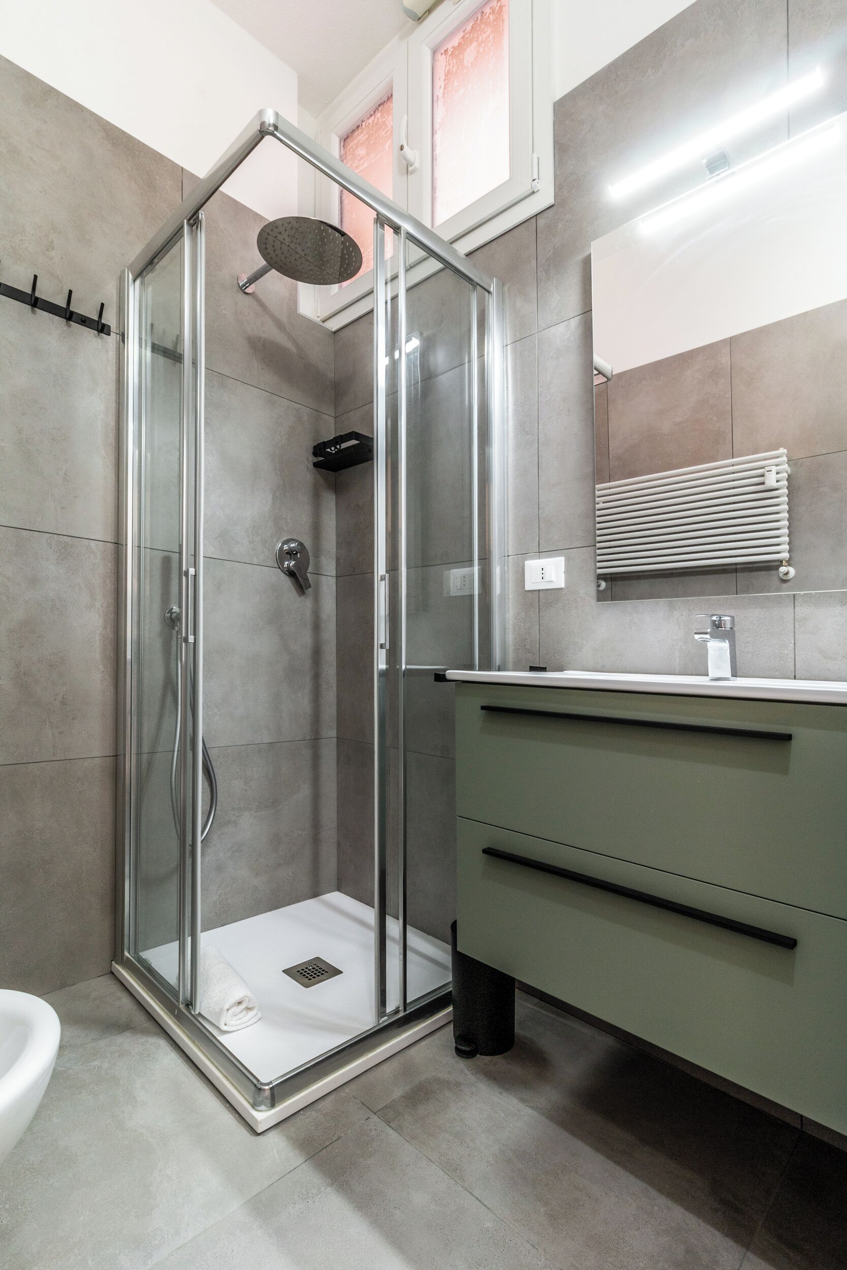 Un baño moderno con ducha acristalada, tocador verde y lavamanos blanco.
