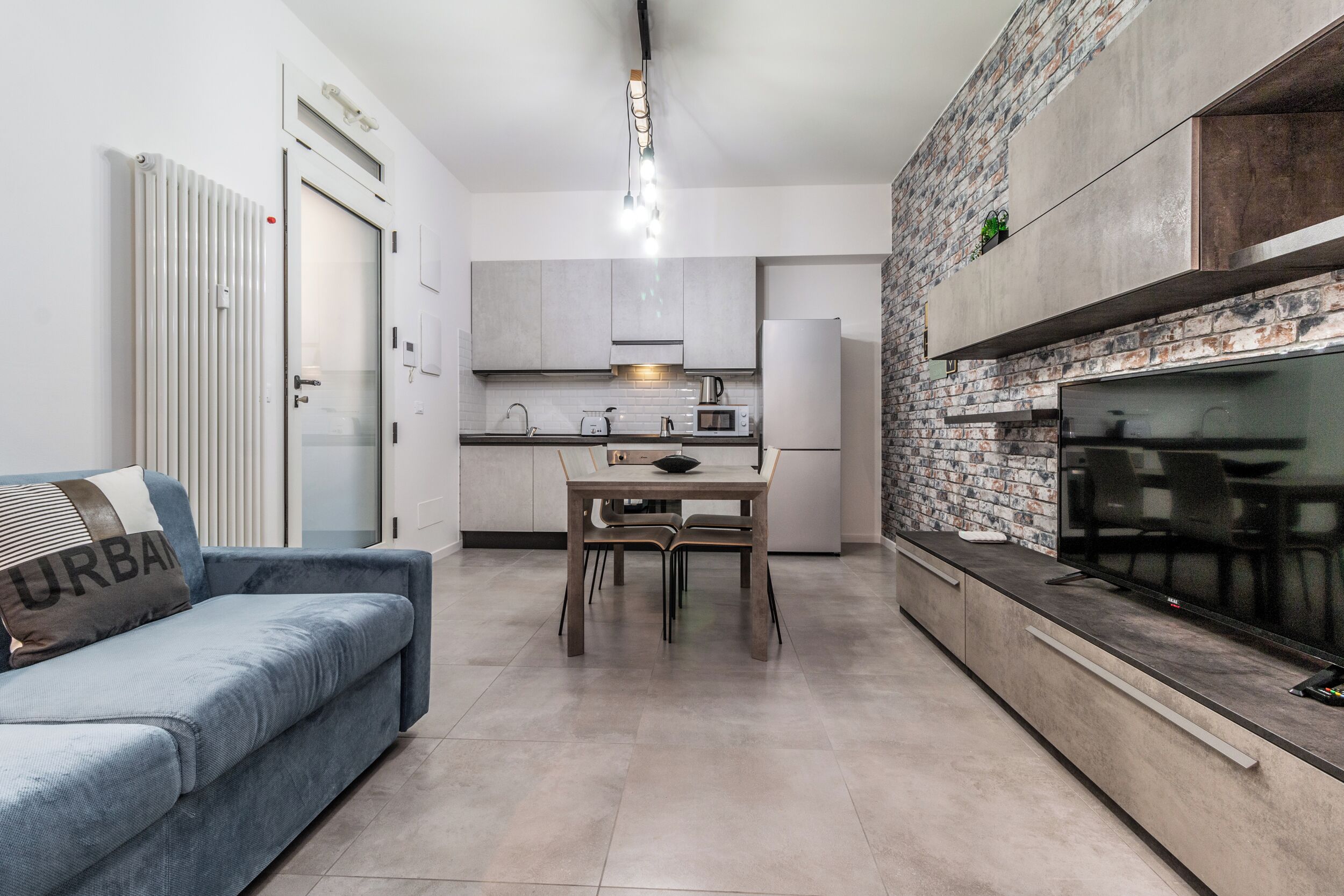 A modern kitchen with a dining area, a sofa, and a TV.