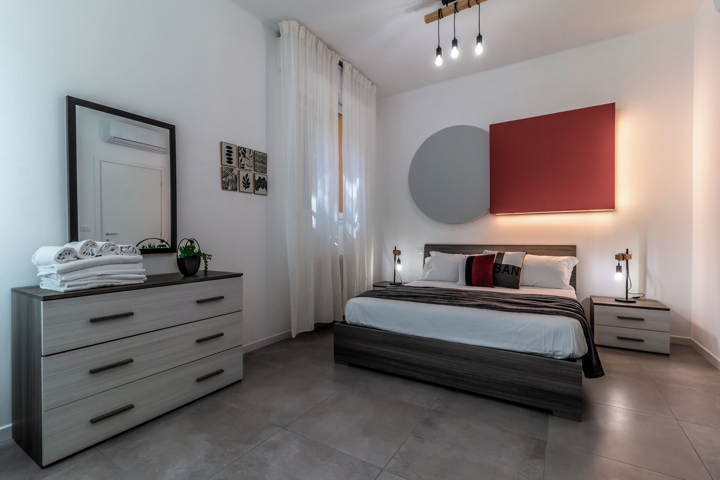 Een moderne slaapkamer met een bed, nachtkastjes, een dressoir, een spiegel en een rode accentmuur.