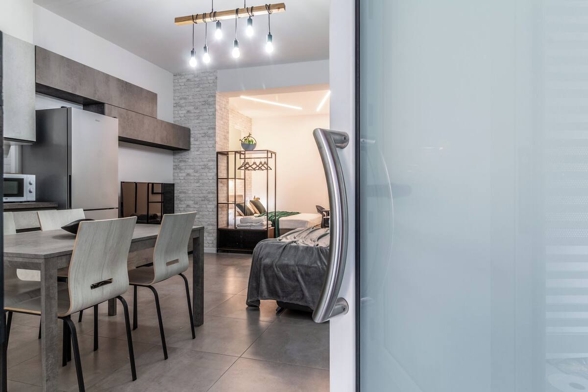 A modern kitchen with a dining area, a bed with a view, and a glass partition.