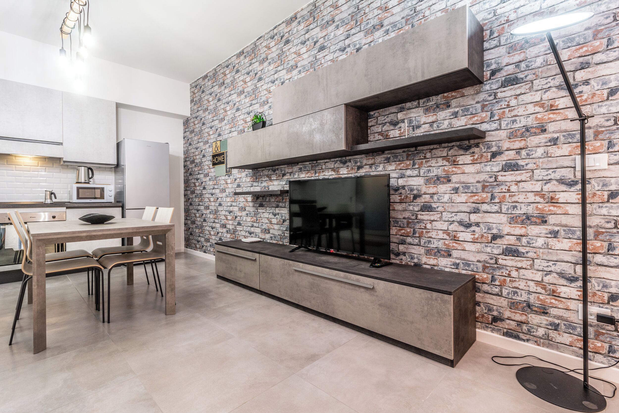 A modern kitchen with a brick wall, a dining area with a table and chairs, and a built-in TV.