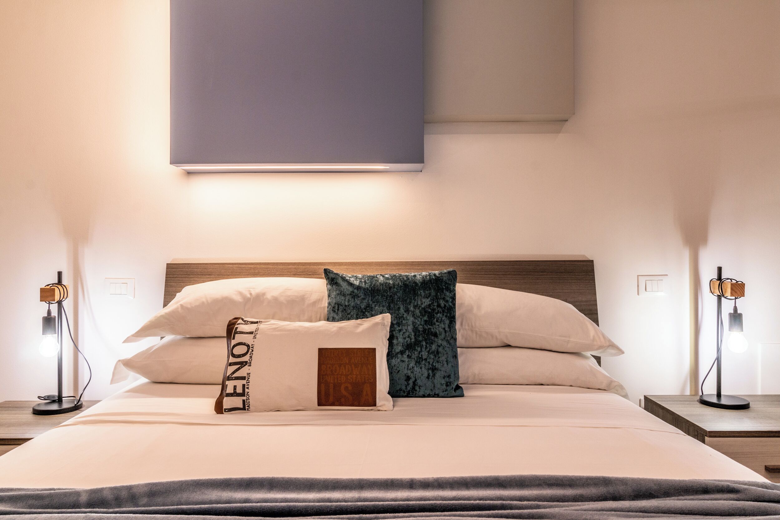 Ein ordentlich bezogenes Bett mit Kopfteil, zwei Nachttischlampen und einer Wandleuchte.