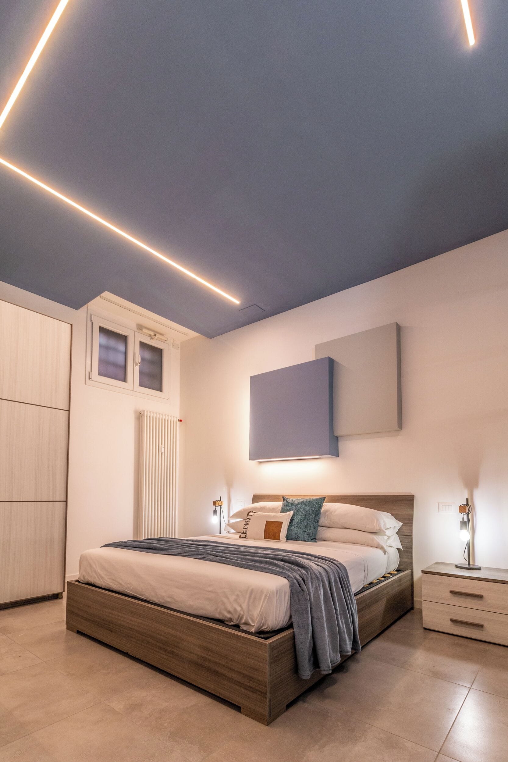 A modern bedroom with a bed, bedside tables, a radiator, and a window.