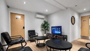 A room with a flat-screen TV, a potted plant, and a seating area with chairs and tables. - Suite with 2 Queen Beds | Downtown Quebec City (Québec City)