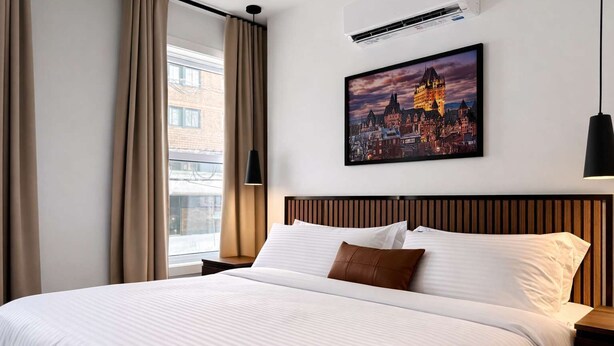 Una camera d'albergo con un letto grande, un dipinto che raffigura una veduta cittadina, un condizionatore d'aria e una finestra con tende.