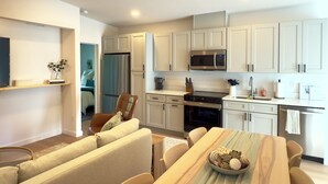 A modern kitchen with white cabinets, a stainless steel refrigerator, a microwave, and a dining area with a wooden table and chairs. - Red Door Retreat- 1 mile to downtown St. Augustine! Pet-friendly! New on market! (St. Augustine)