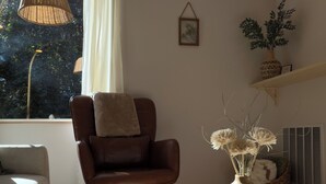 A living room with a brown leather chair, a round glass coffee table, a bookshelf with decorative items, and a window with curtains. - Red Door Retreat- 1 mile to downtown St. Augustine! Pet-friendly! New on market! (St. Augustine)