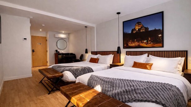 A hotel room with two beds, a bench, a desk, a chair, and a large window. - Room with 2 Queen Beds | Downtown Quebec City (Québec City)