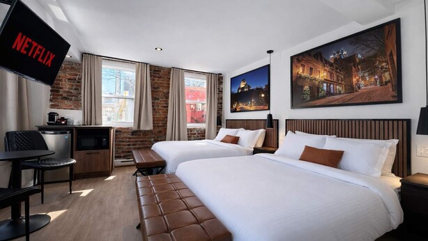 Ein Hotelzimmer mit zwei Betten, einem Schreibtisch, einem Fernseher und einer Sitzbank.