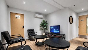 Ein Zimmer mit Flachbildfernseher, einem Blumentopf und einer Sitzecke mit Stühlen und Tischen.