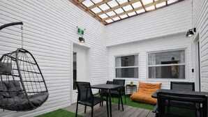 Een overdekt terras met een hangstoel, een tafel met stoelen en een bank.